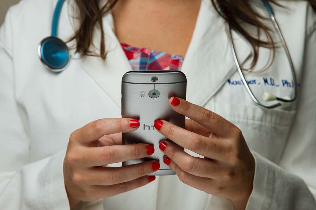 Seeking: Women’s Digital Health Startups-Image of a female doctor in coat with stethoscope and bright red lab coat holding an htc smartphone with both hands. 