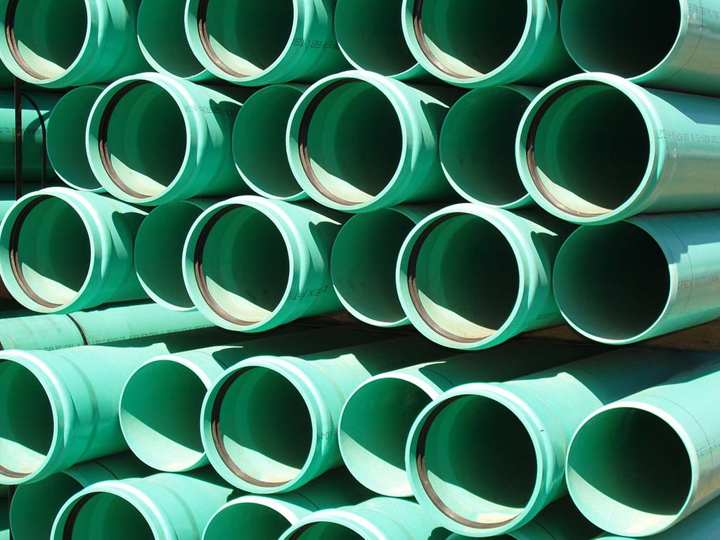 Improved Durability of Plastic Parts-Image end on of a stack of large green pipes with black gaskets in the flange