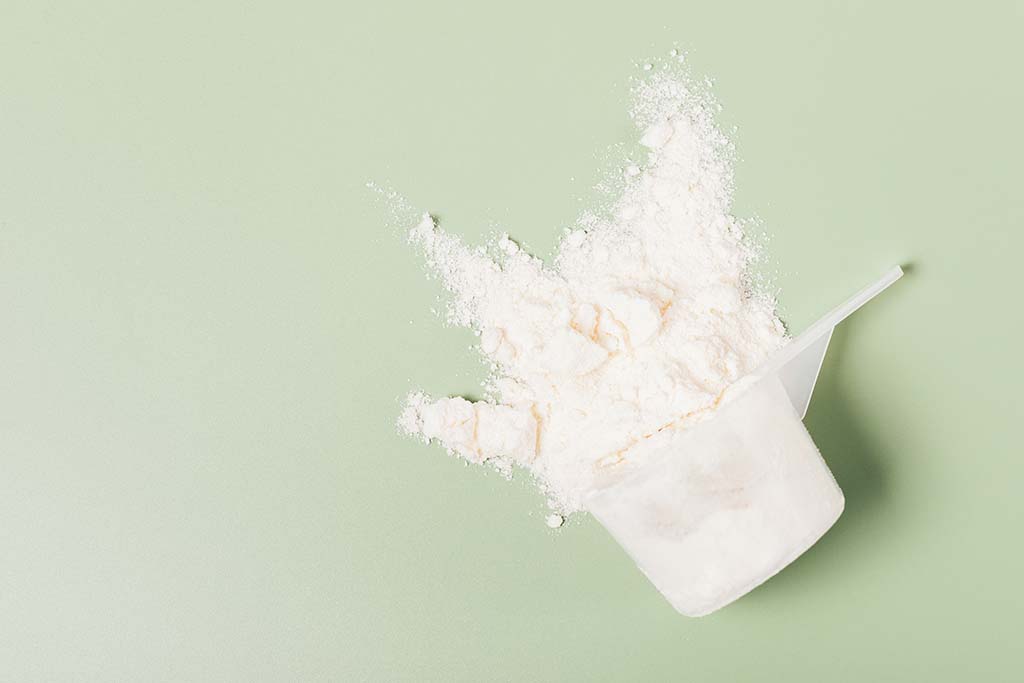 PepsiCo Seeking: Novel Protein Solutions for Beverages-Image of protein powder in a measuring cup spilled on a light green background