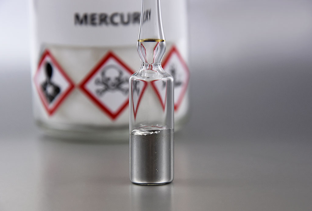 A white metal in a vial in the foreground and bottle labelled mercury in the background with symbols for poison and other warning labels