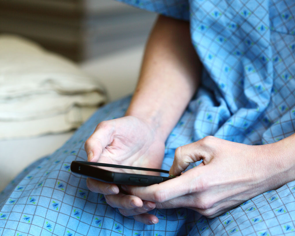 patient in a blue hospital gown holding a cell phone while sitting